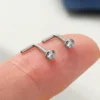 Two silver-tone L-shaped nose studs resting on a fingertip, showing their small size