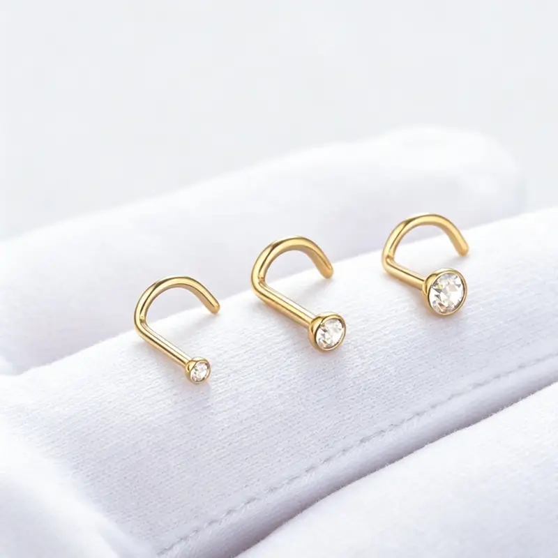 Three gold-tone CZ nose screws on white fabric, shown in different stone sizes