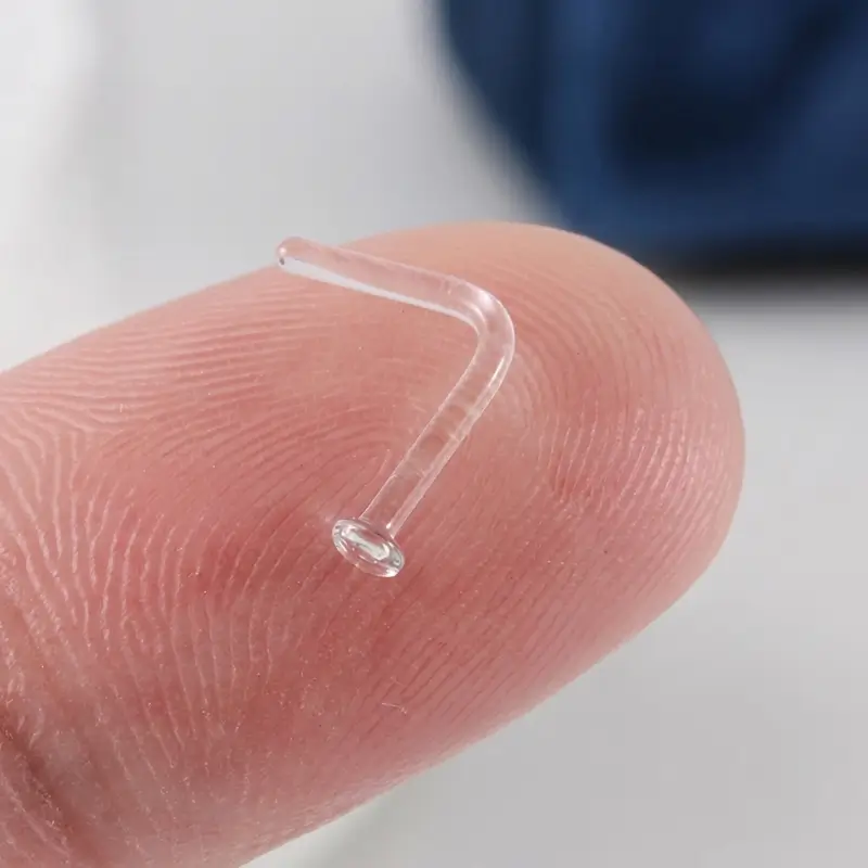glass-nose-stud-on-fingertip Clear glass L-shaped nose stud resting on a fingertip, showing its small size
